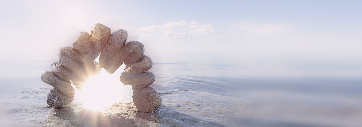 Steintor aus einzelnen Steinen am Stand mit Meer im Hintergrund und das Sonnenlicht fällt durch dieses Tor